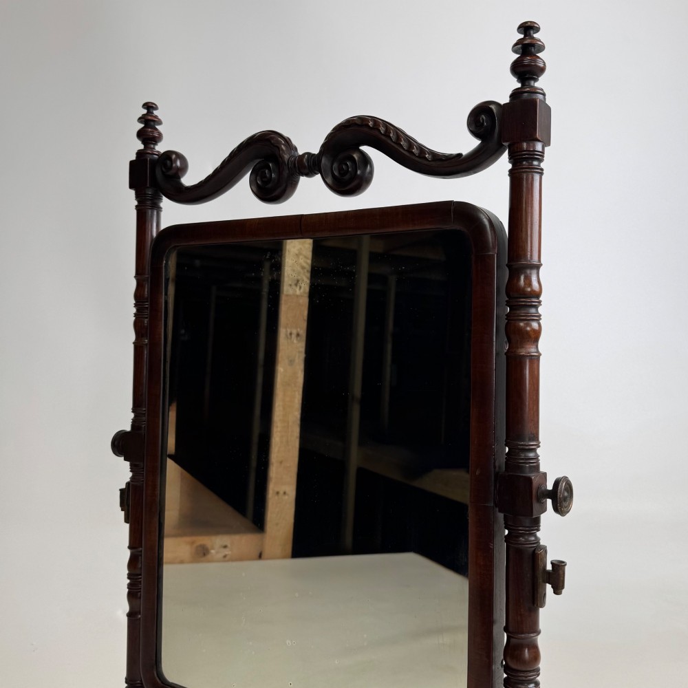 A 19th-century mahogany dressing mirror with turned side columns, carved scrollwork cresting, and an adjustable rectangular glass frame on a shaped base. View XII