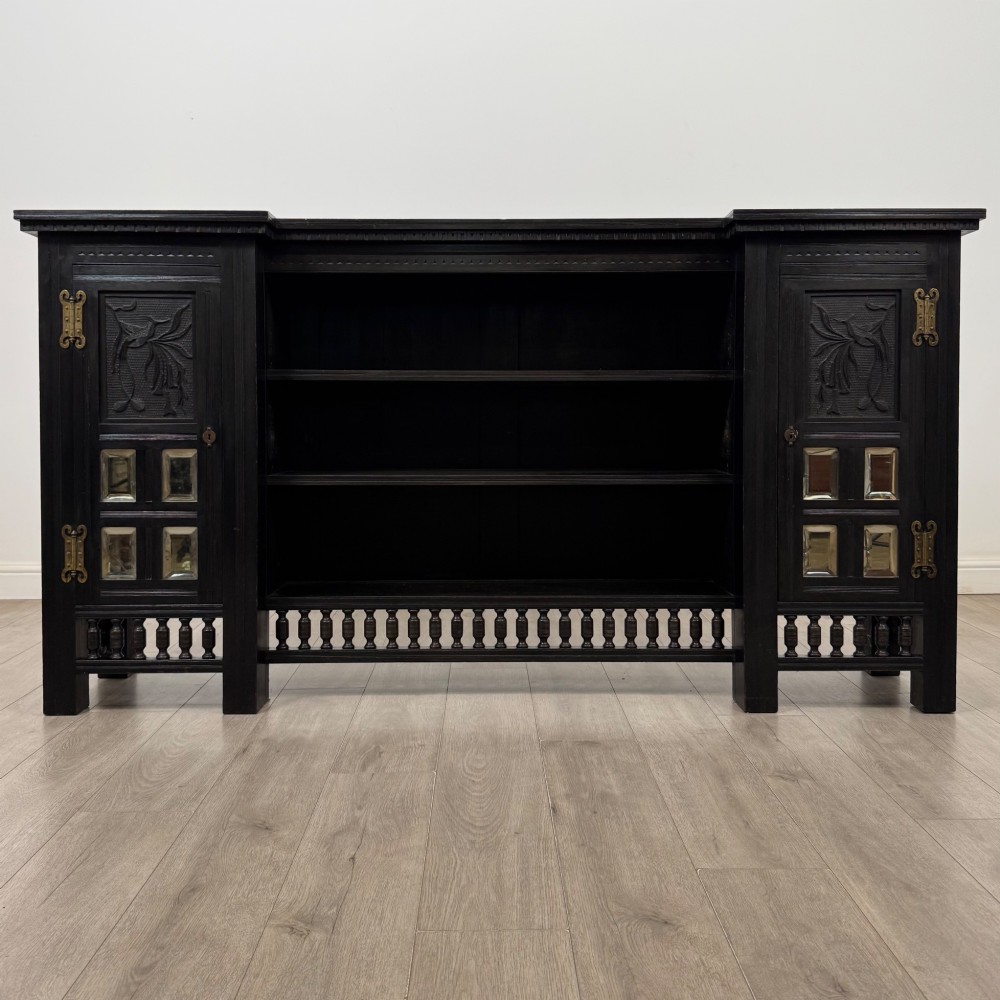 An antique ebonised black wood sideboard featuring a central open bookshelf, two carved side doors with glass panels, brass hardware, and a spindled lower rail. View II