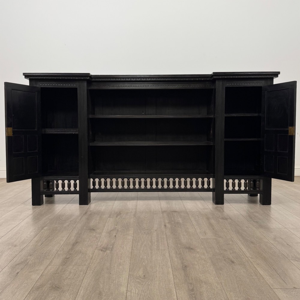 An antique ebonised black wood sideboard featuring a central open bookshelf, two carved side doors with glass panels, brass hardware, and a spindled lower rail. View III