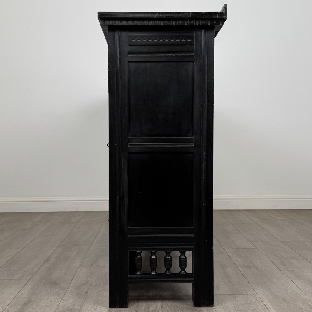 An antique ebonised black wood sideboard featuring a central open bookshelf, two carved side doors with glass panels, brass hardware, and a spindled lower rail. View V