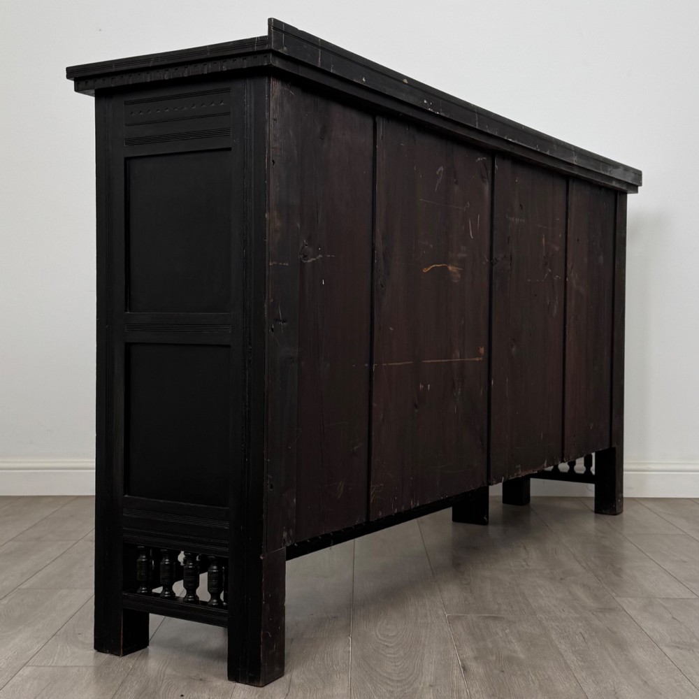 An antique ebonised black wood sideboard featuring a central open bookshelf, two carved side doors with glass panels, brass hardware, and a spindled lower rail. View VI