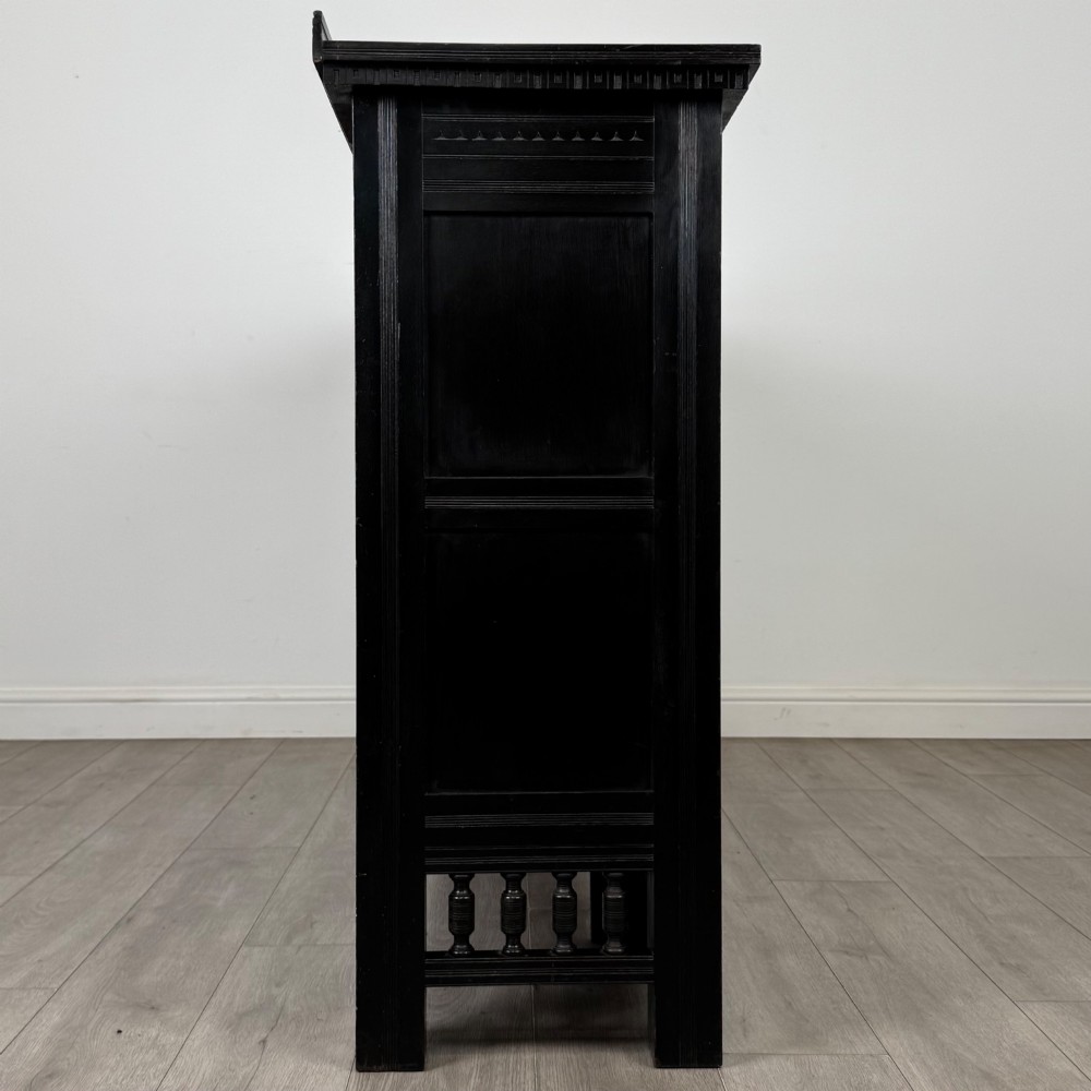 An antique ebonised black wood sideboard featuring a central open bookshelf, two carved side doors with glass panels, brass hardware, and a spindled lower rail. View IX