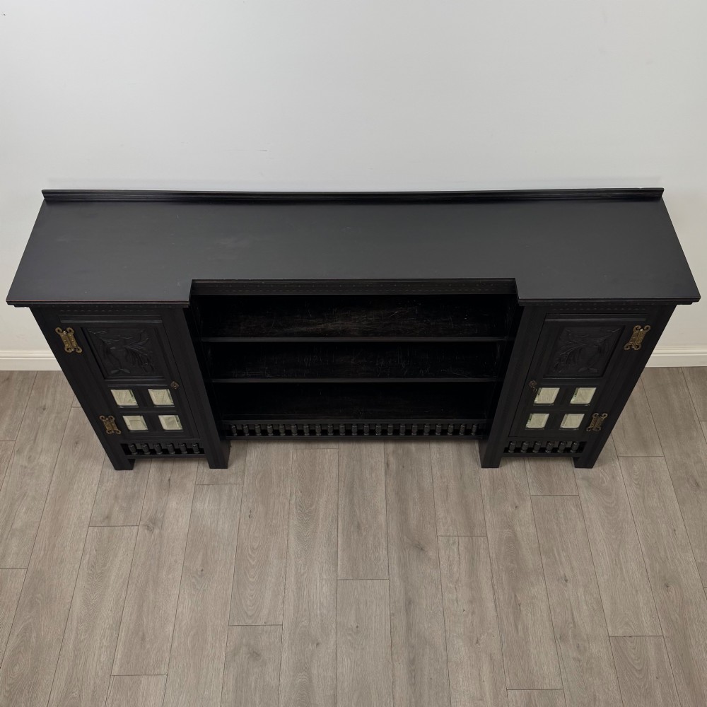 An antique ebonised black wood sideboard featuring a central open bookshelf, two carved side doors with glass panels, brass hardware, and a spindled lower rail. View XI