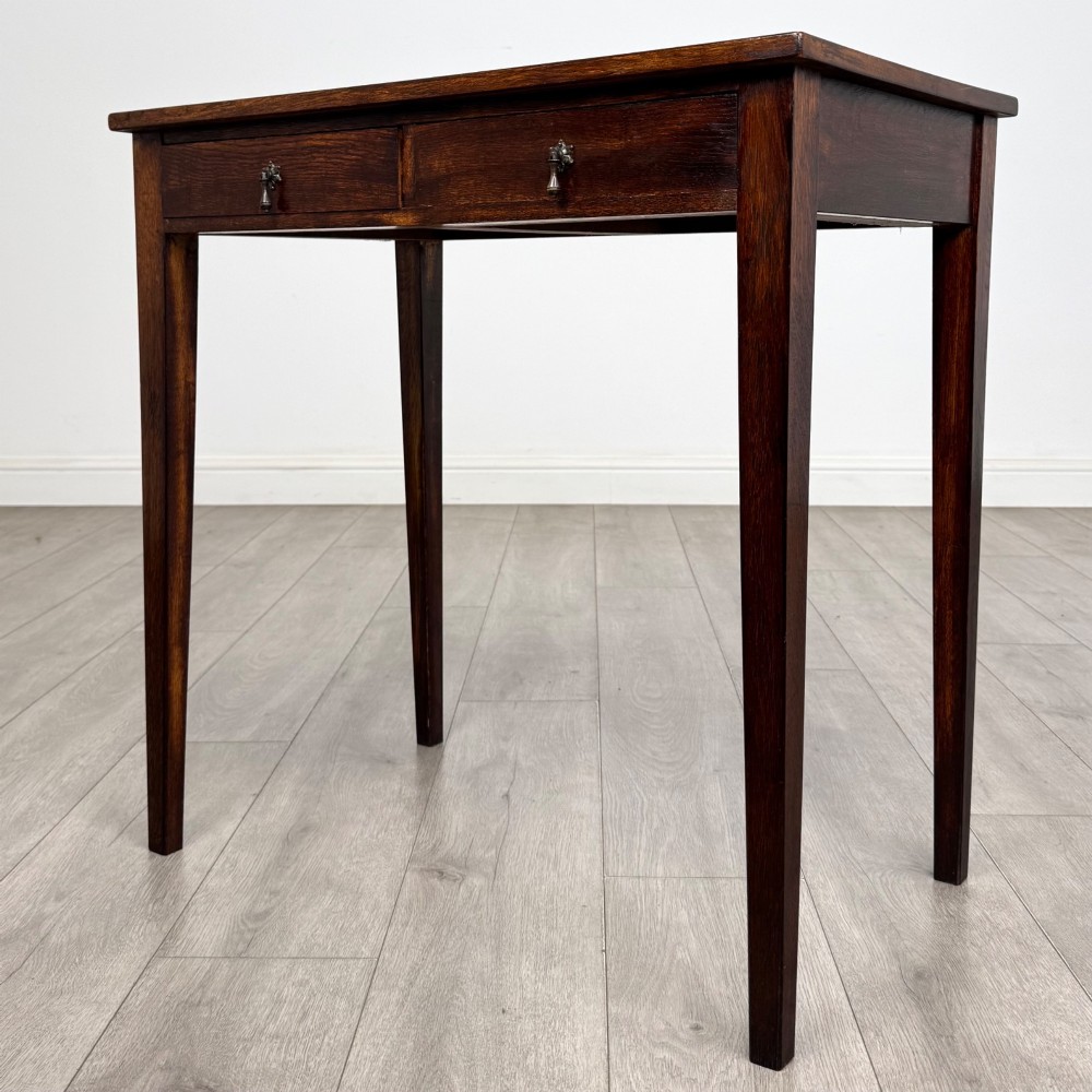 An antique dark oak Edwardian side table with two front drawers, metallic drop handles, and straight tapered legs. View II