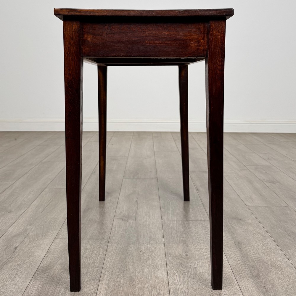 An antique dark oak Edwardian side table with two front drawers, metallic drop handles, and straight tapered legs. View III