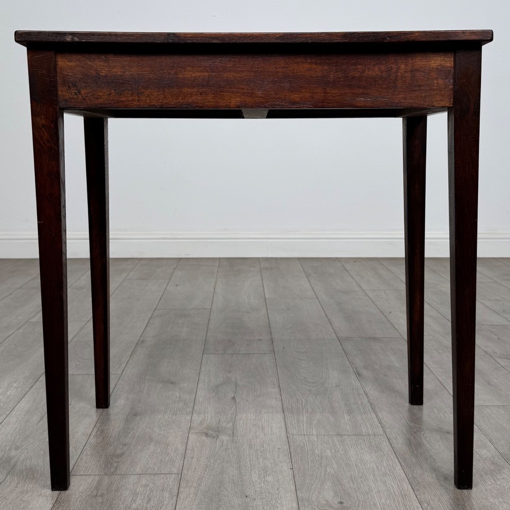 An antique dark oak Edwardian side table with two front drawers, metallic drop handles, and straight tapered legs. View V