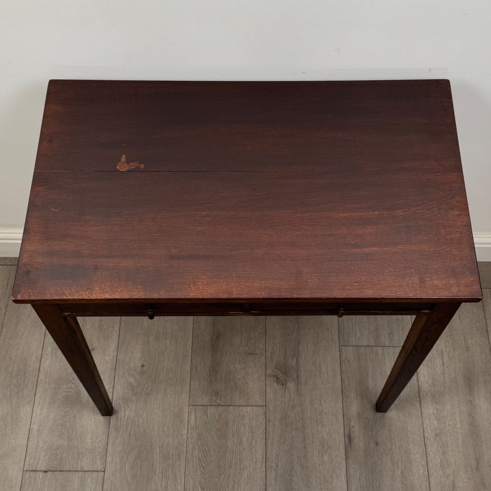 An antique dark oak Edwardian side table with two front drawers, metallic drop handles, and straight tapered legs. View IX