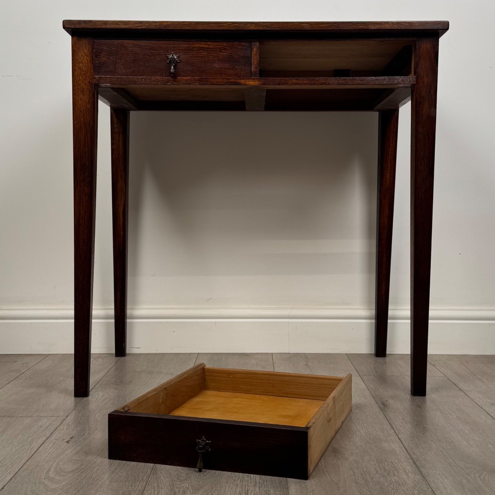 An antique dark oak Edwardian side table with two front drawers, metallic drop handles, and straight tapered legs. View X