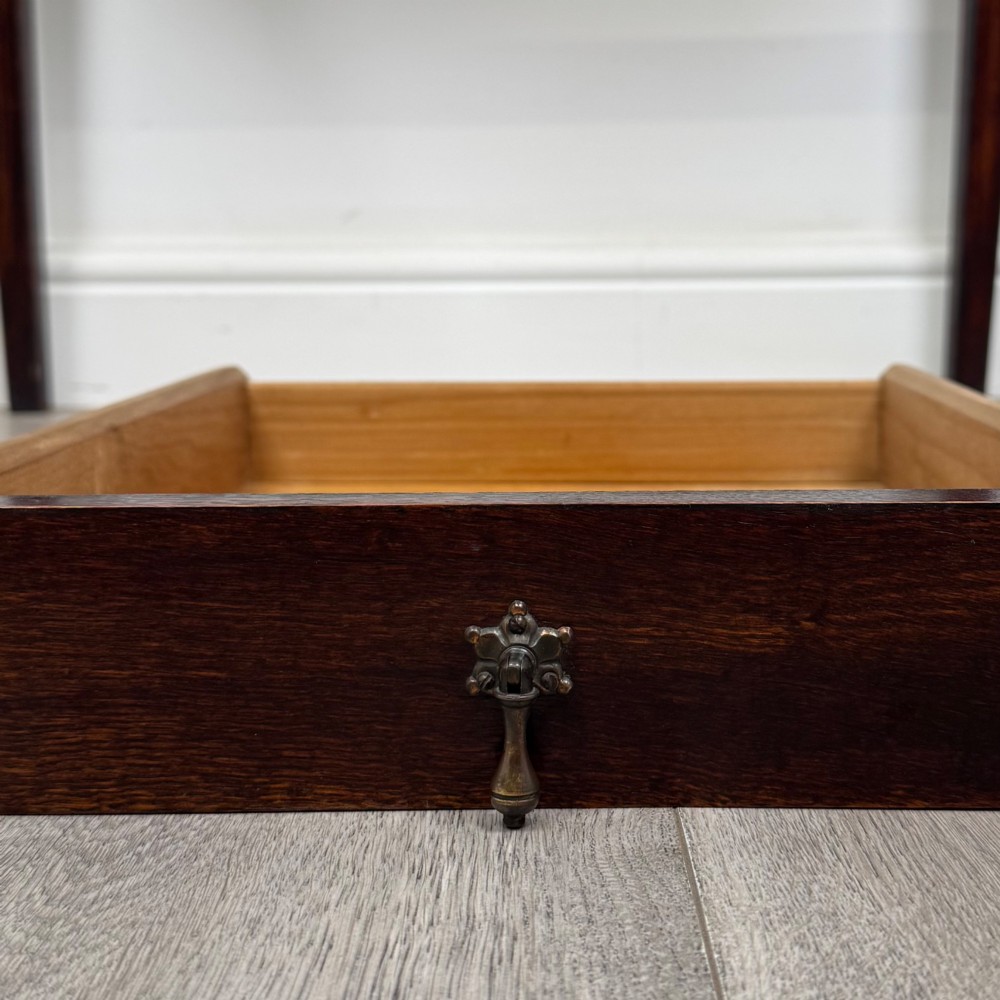 An antique dark oak Edwardian side table with two front drawers, metallic drop handles, and straight tapered legs. View XI