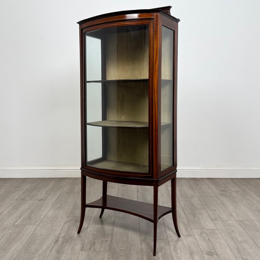 An Edwardian mahogany display cabinet with a bow-front glazed door, fabric-lined interior shelves, marquetry inlay, and slender tapered legs with a lower shelf. View III