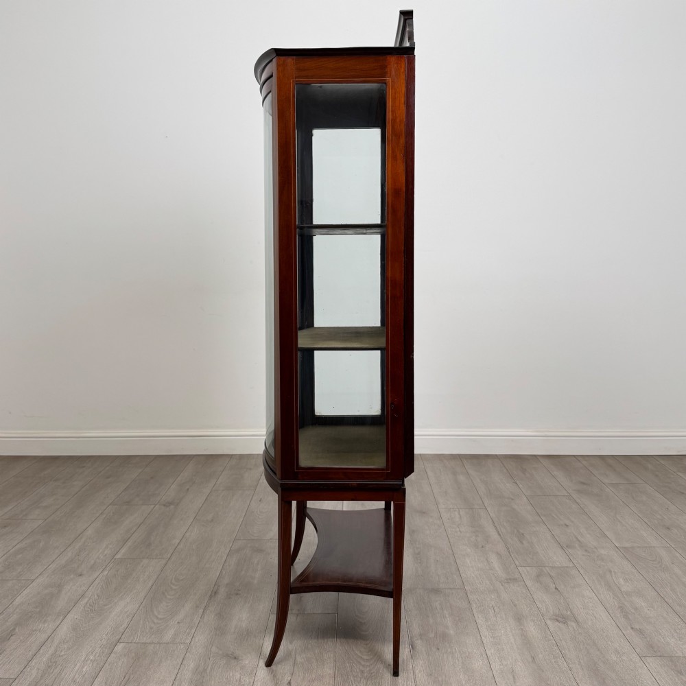 An Edwardian mahogany display cabinet with a bow-front glazed door, fabric-lined interior shelves, marquetry inlay, and slender tapered legs with a lower shelf. View IV