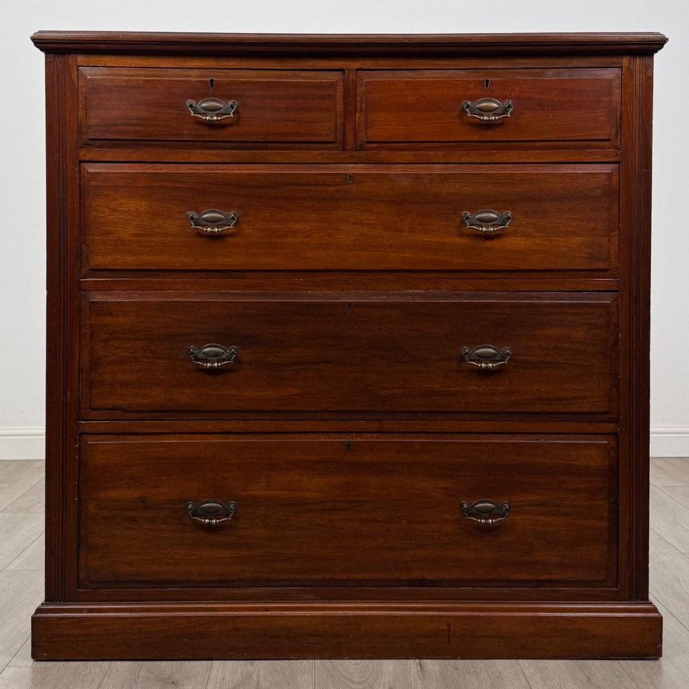 An Edwardian walnut chest of drawers featuring a two over three drawer layout with brass drop handles and a solid plinth base.