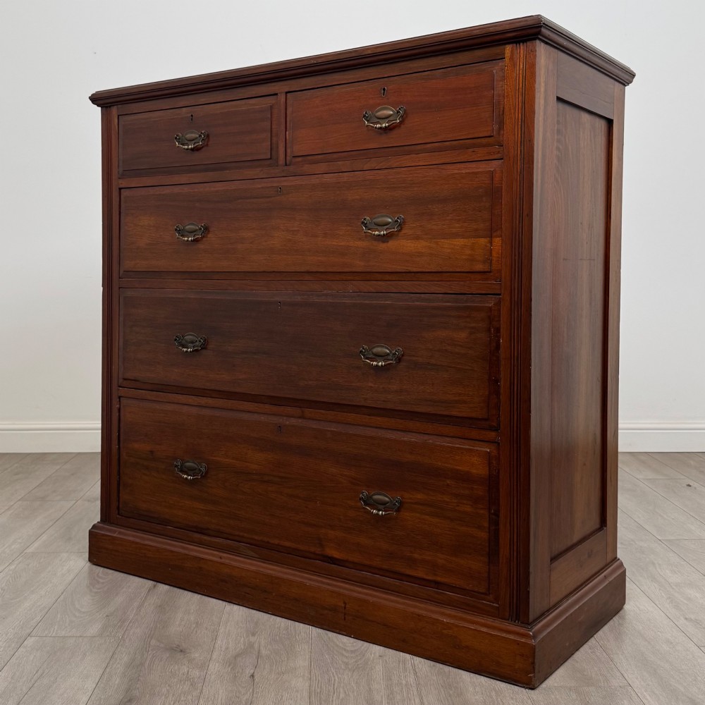 An Edwardian walnut chest of drawers featuring a two over three drawer layout with brass drop handles and a solid plinth base. View II