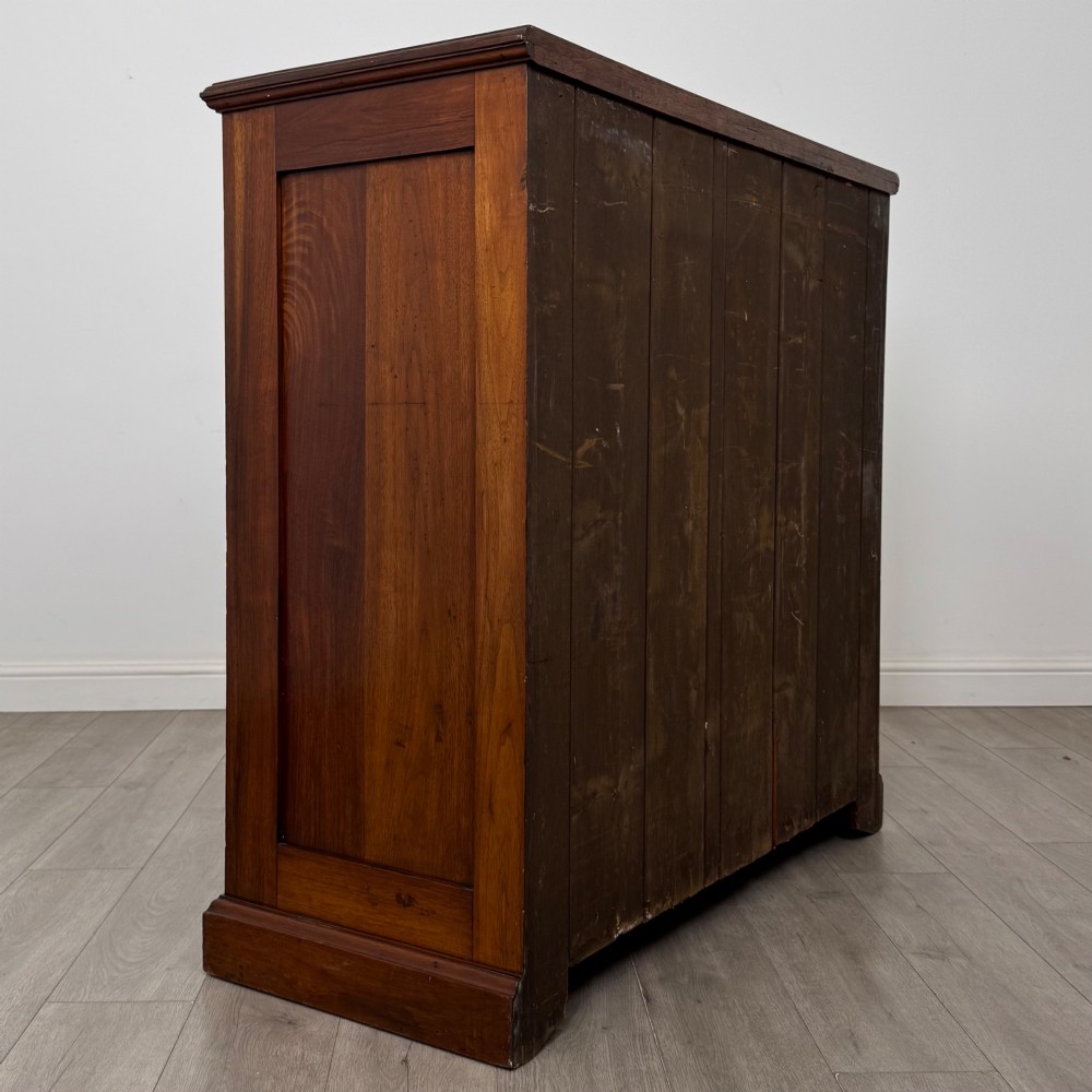 An Edwardian walnut chest of drawers featuring a two over three drawer layout with brass drop handles and a solid plinth base. View IV