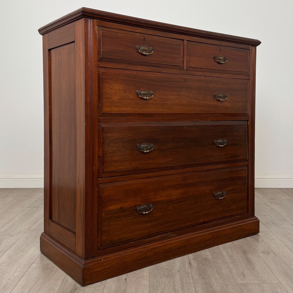 An Edwardian walnut chest of drawers featuring a two over three drawer layout with brass drop handles and a solid plinth base. View VIII