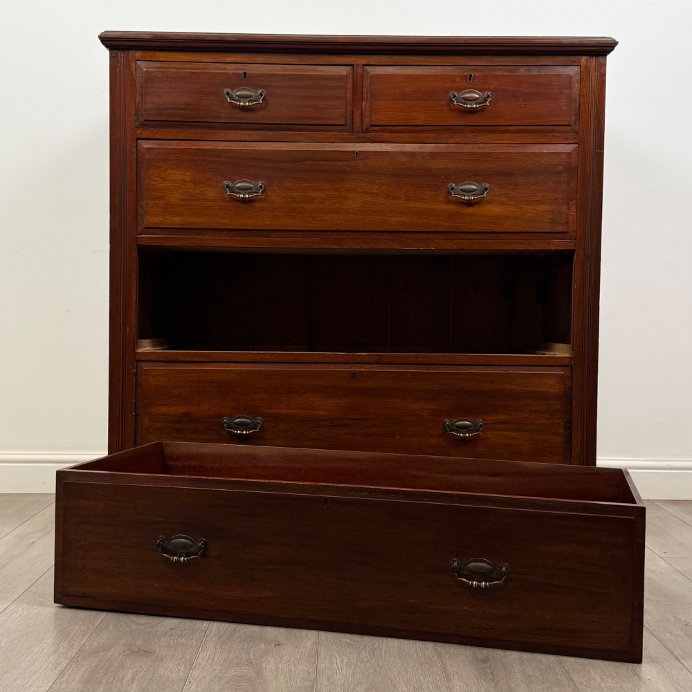 An Edwardian walnut chest of drawers featuring a two over three drawer layout with brass drop handles and a solid plinth base. View X