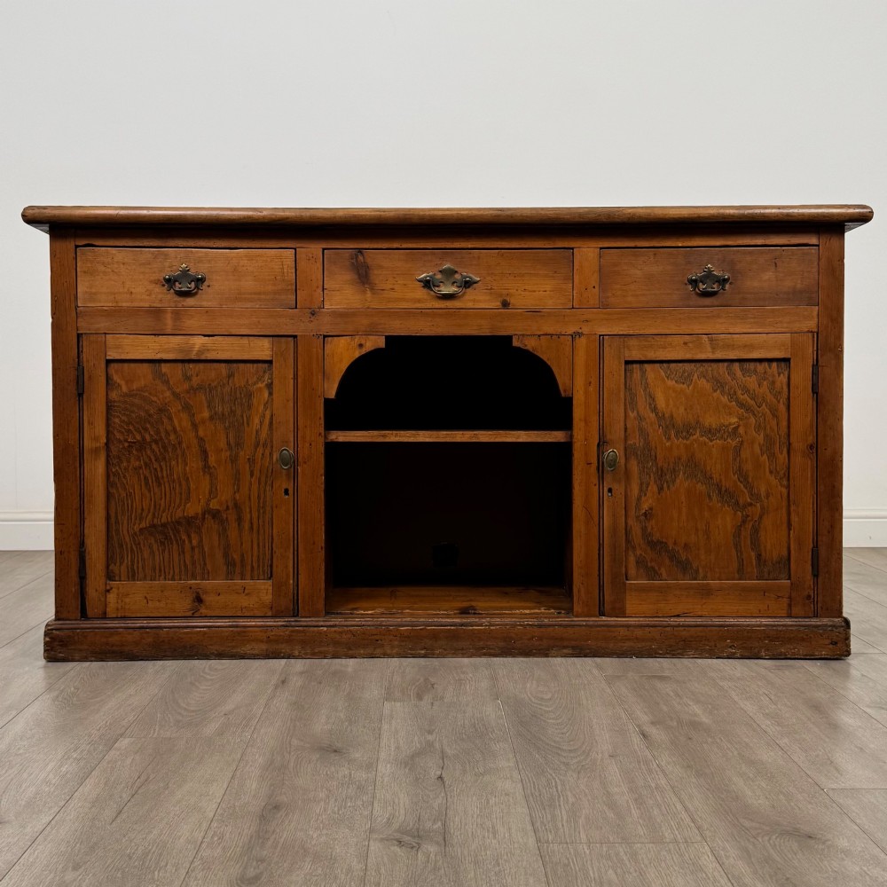 A 19th-century pine farmhouse dresser base featuring three upper drawers above two cupboard doors and an open central shelf.