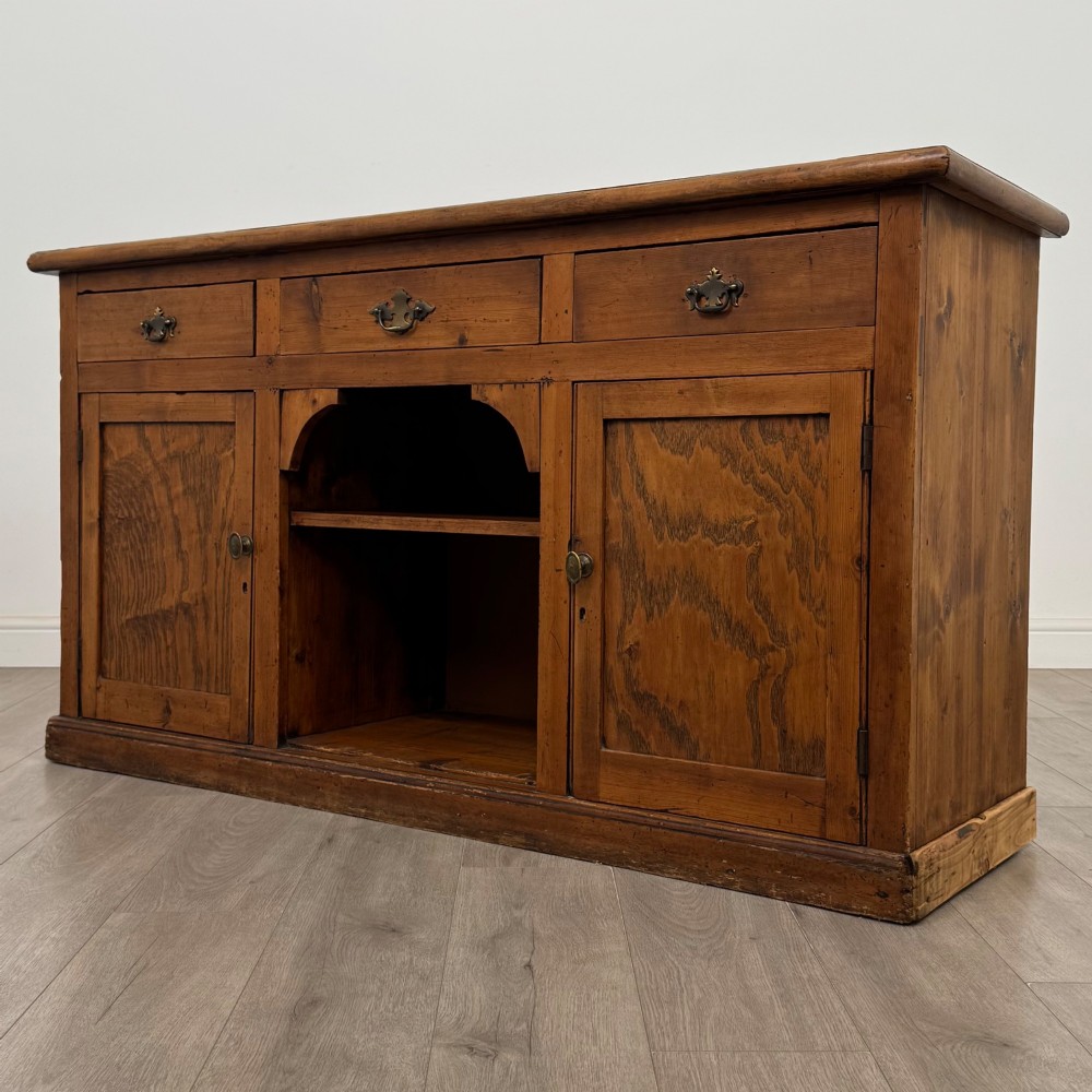 A 19th-century pine farmhouse dresser base featuring three upper drawers above two cupboard doors and an open central shelf. View III