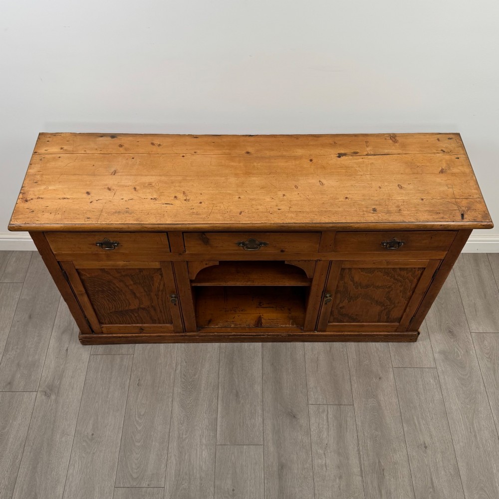 A 19th-century pine farmhouse dresser base featuring three upper drawers above two cupboard doors and an open central shelf. View X