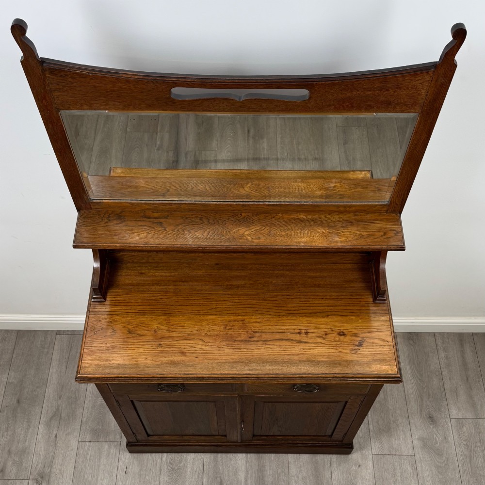 An early 20th-century warm brown oak mirror back sideboard featuring two drawers, a double-door cupboard base, and an elevated mirror plate cresting. View X