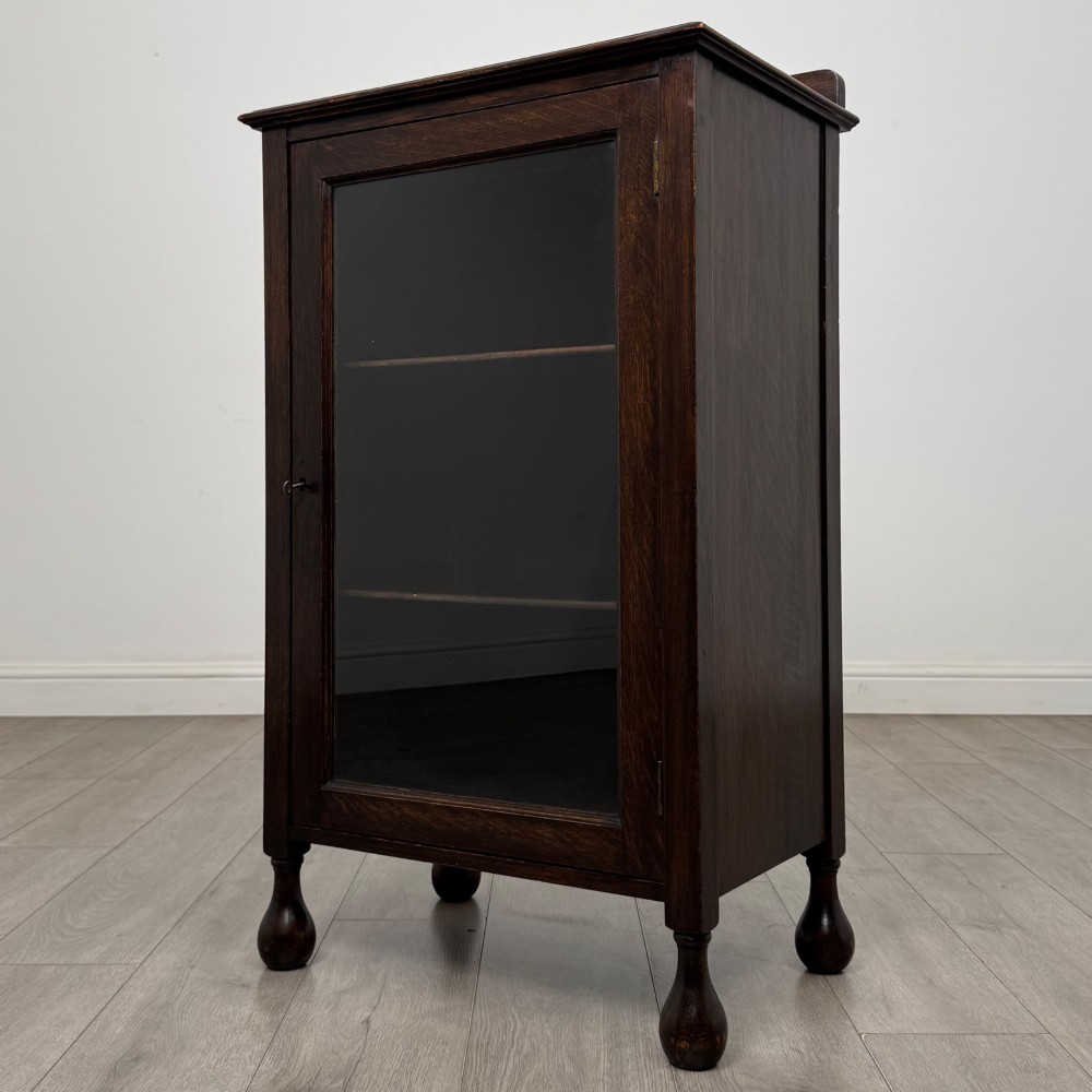 An Edwardian dark brown oak display cabinet featuring a single glazed door and turned feet. View III