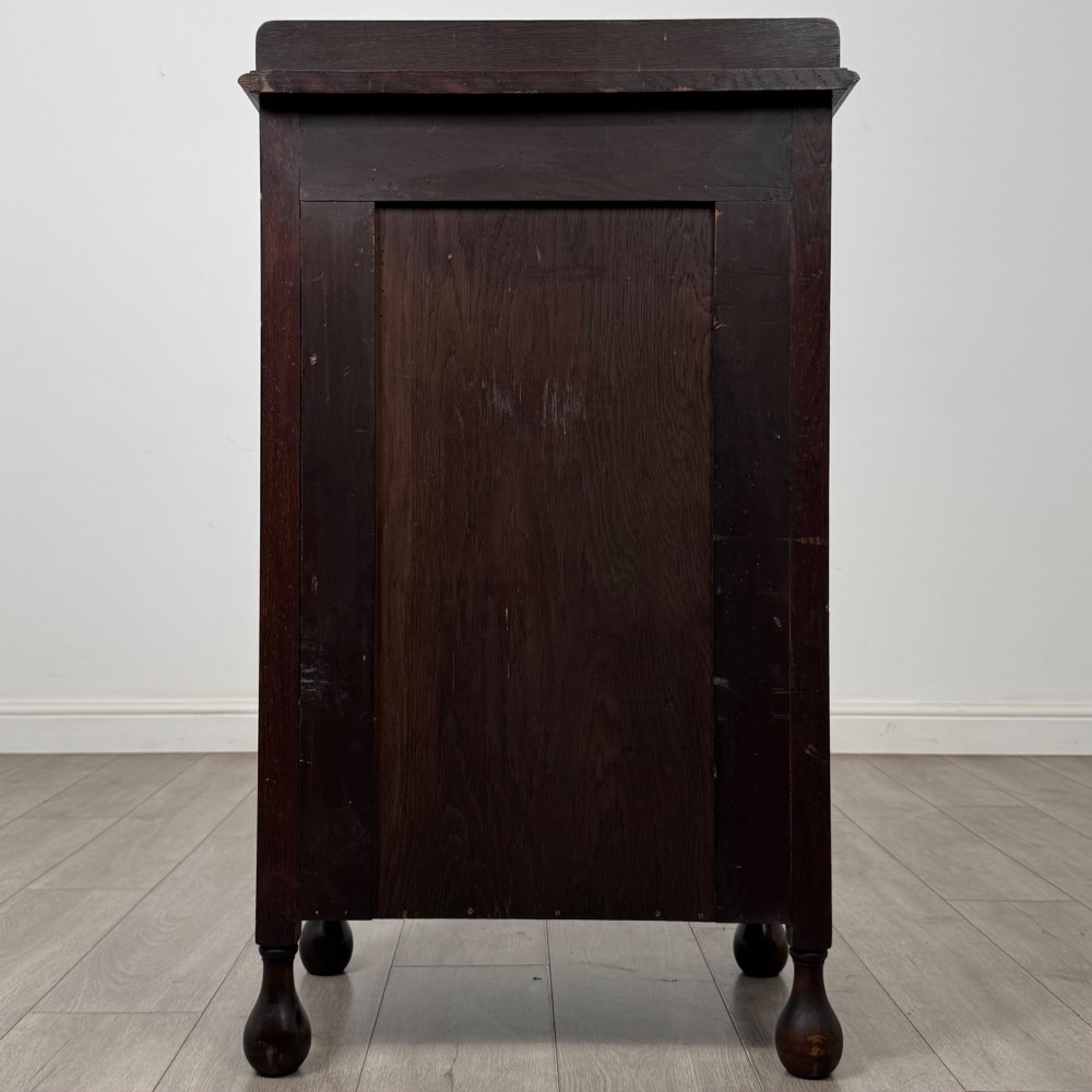 An Edwardian dark brown oak display cabinet featuring a single glazed door and turned feet. View VI