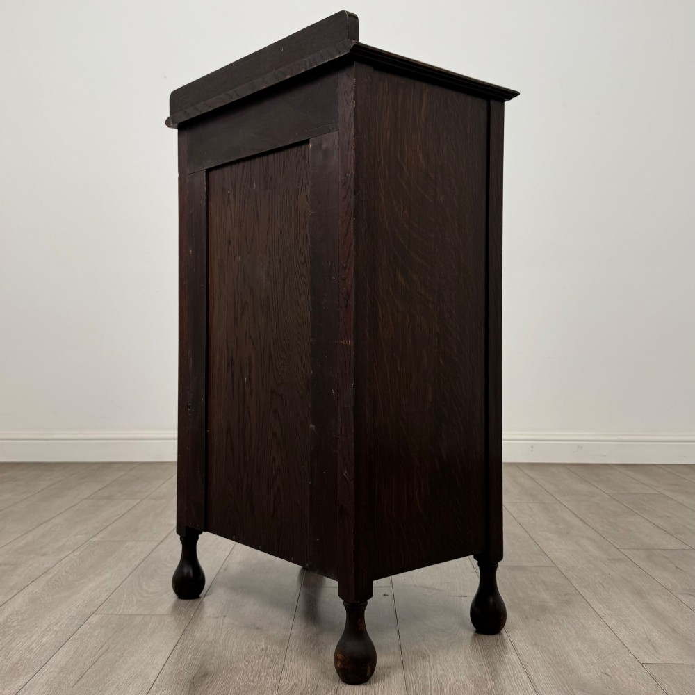 An Edwardian dark brown oak display cabinet featuring a single glazed door and turned feet. View VII