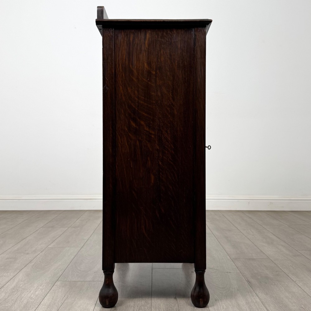 An Edwardian dark brown oak display cabinet featuring a single glazed door and turned feet. View VIII