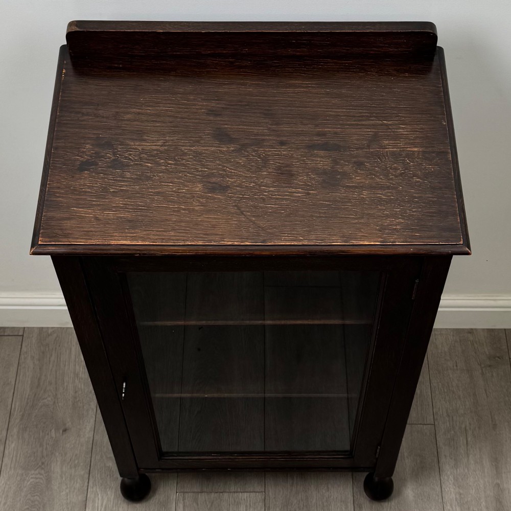 An Edwardian dark brown oak display cabinet featuring a single glazed door and turned feet. View X
