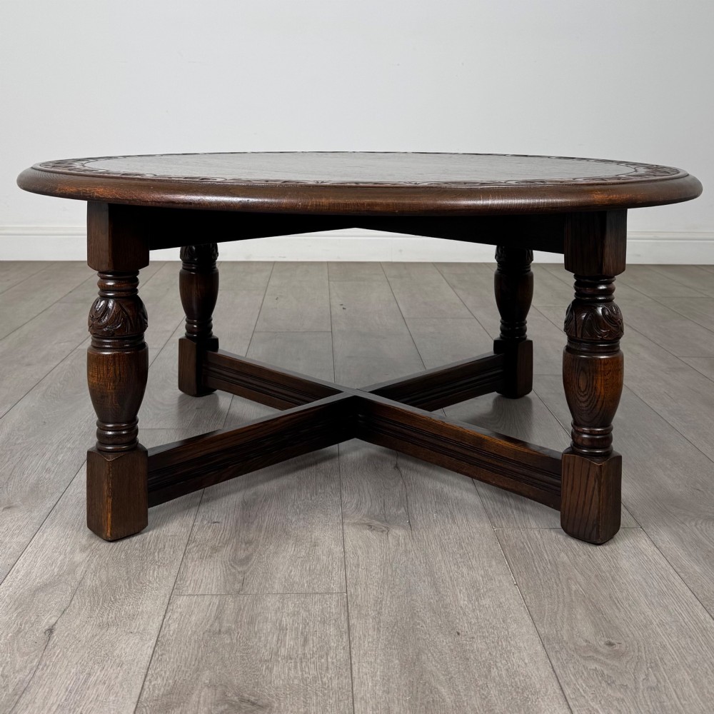 A low circular dark oak coffee table featuring carved turned legs, an X-shaped cross stretcher, and a carved geometric border along the top rim.