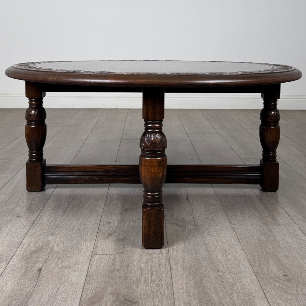 A low circular dark oak coffee table featuring carved turned legs, an X-shaped cross stretcher, and a carved geometric border along the top rim. View III