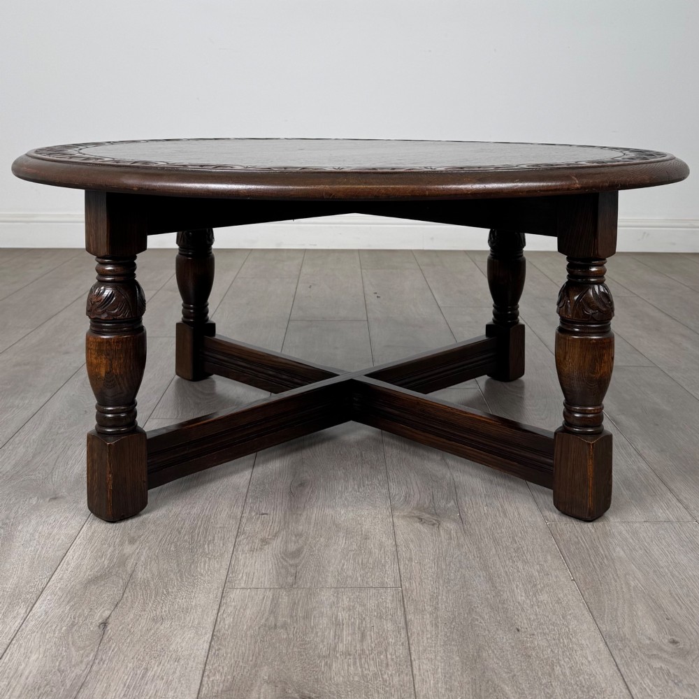 A low circular dark oak coffee table featuring carved turned legs, an X-shaped cross stretcher, and a carved geometric border along the top rim. View IV