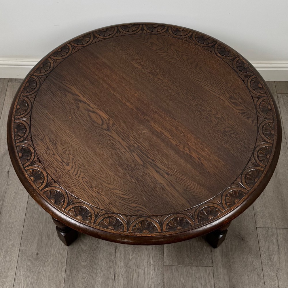 A low circular dark oak coffee table featuring carved turned legs, an X-shaped cross stretcher, and a carved geometric border along the top rim. View VIII
