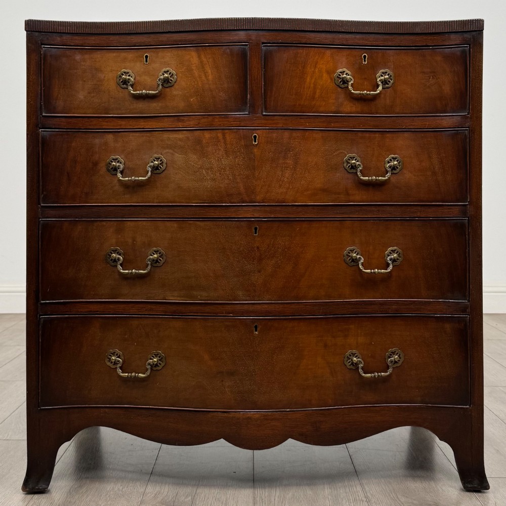 A mahogany serpentine chest of drawers featuring four graduating drawer tiers with brass handles and a curved front profile.