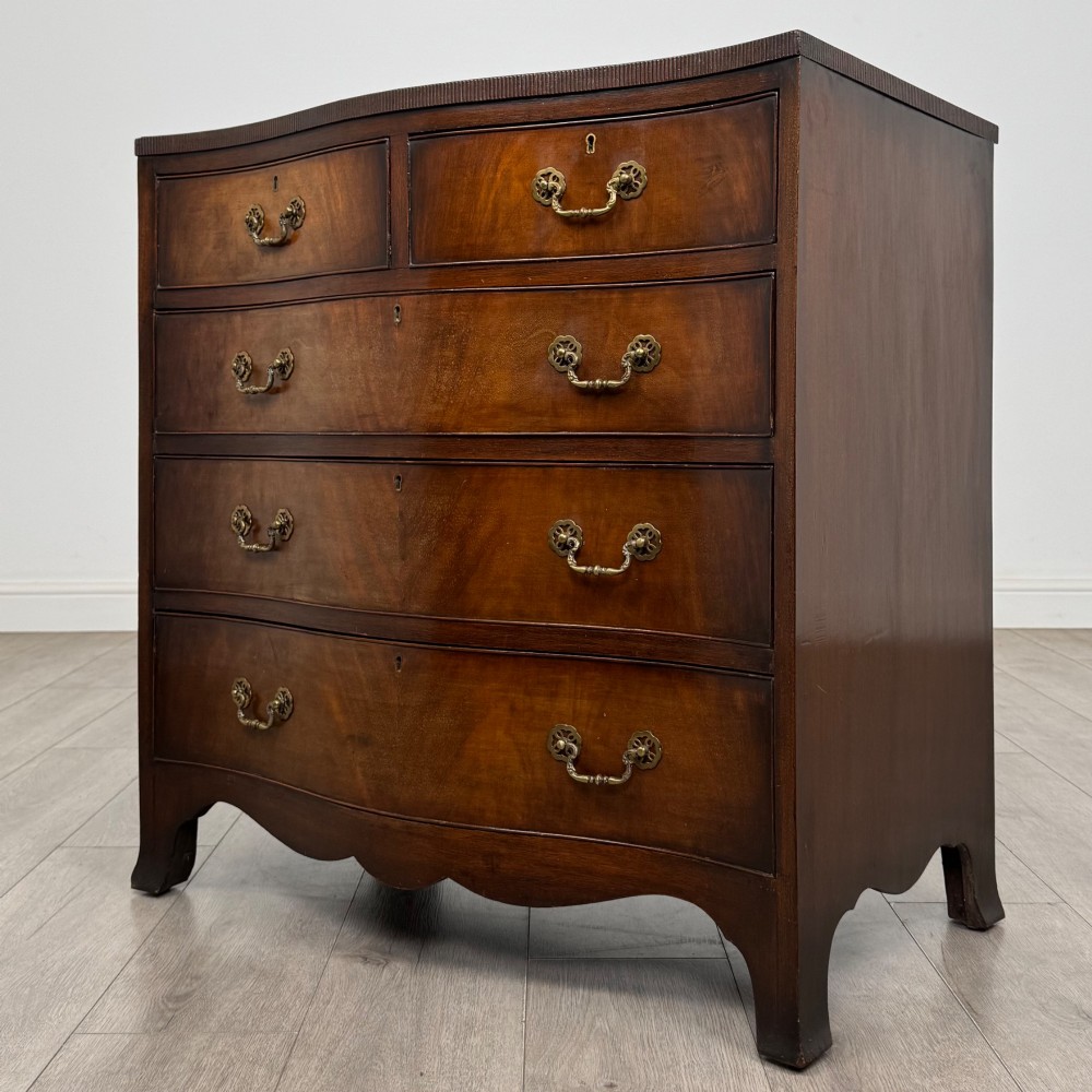 A mahogany serpentine chest of drawers featuring four graduating drawer tiers with brass handles and a curved front profile. View II