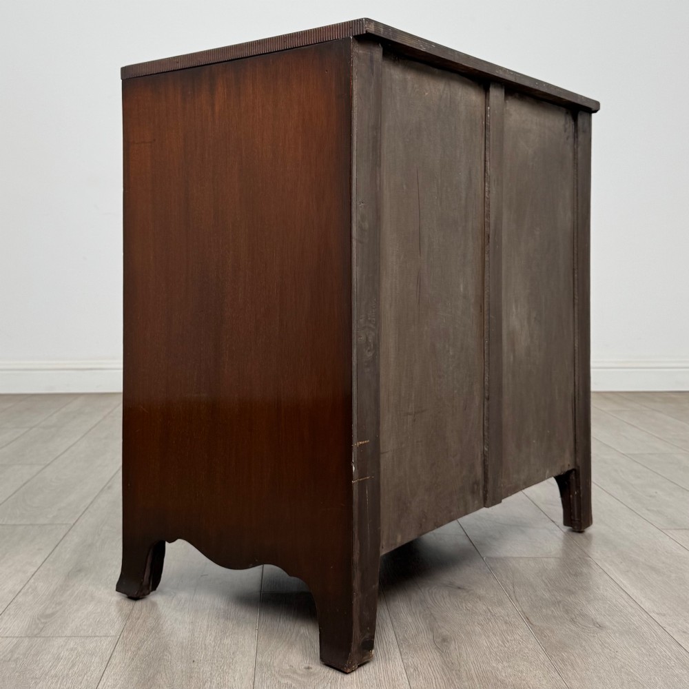 A mahogany serpentine chest of drawers featuring four graduating drawer tiers with brass handles and a curved front profile. View IV