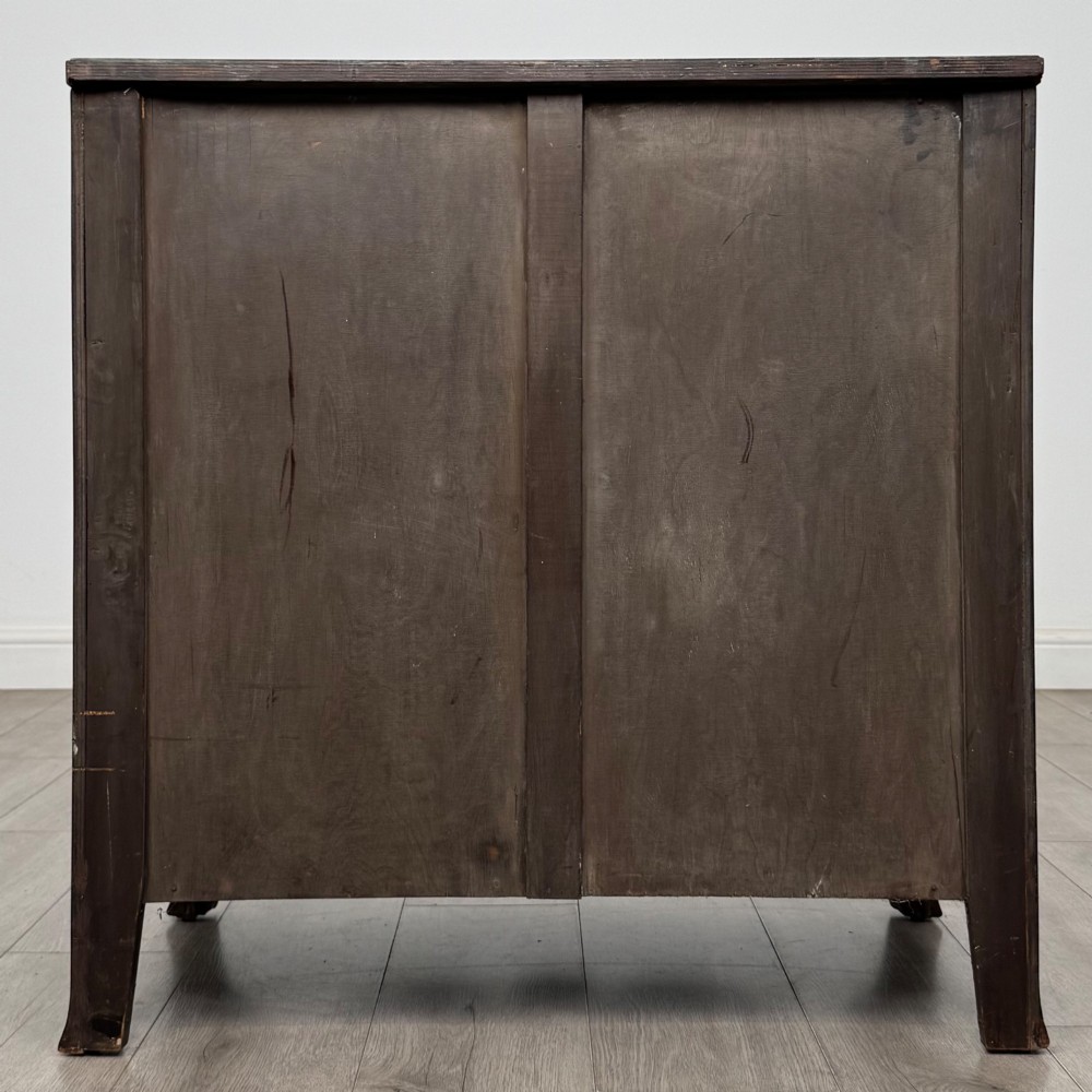 A mahogany serpentine chest of drawers featuring four graduating drawer tiers with brass handles and a curved front profile. View V