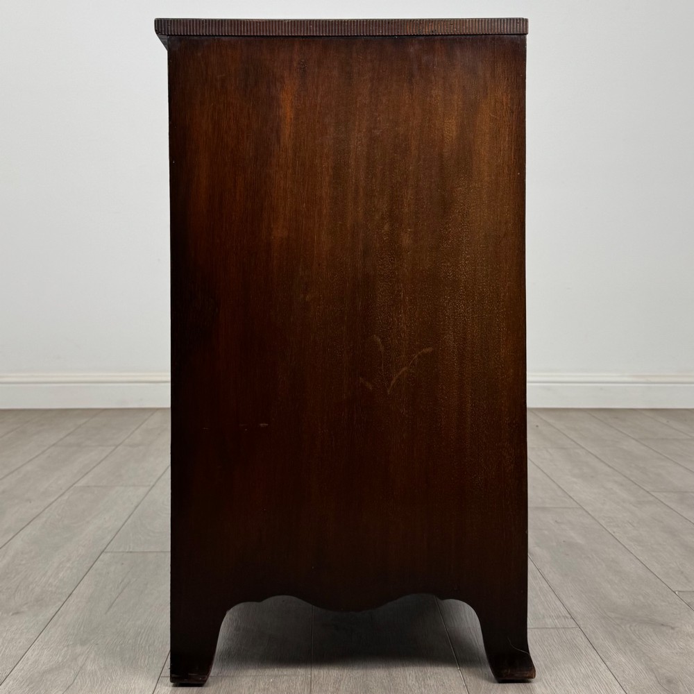 A mahogany serpentine chest of drawers featuring four graduating drawer tiers with brass handles and a curved front profile. View VII