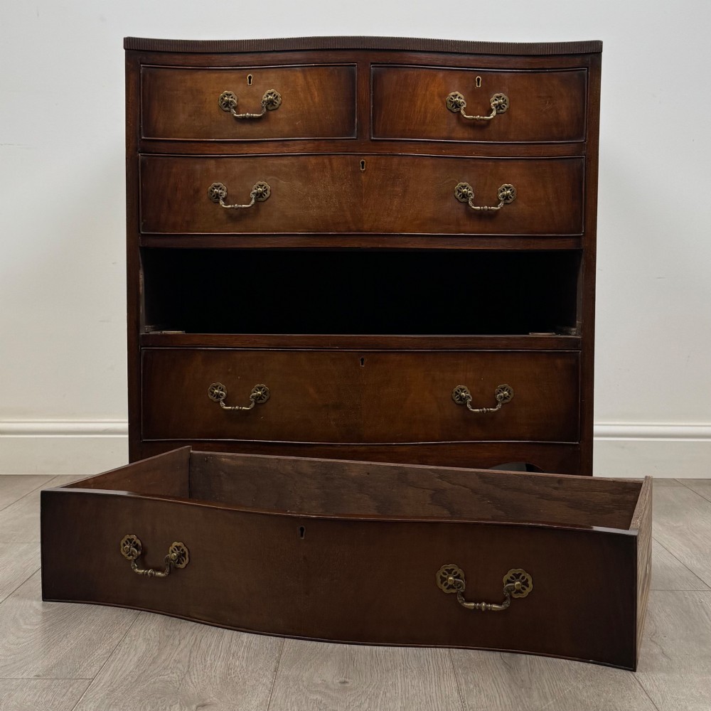 A mahogany serpentine chest of drawers featuring four graduating drawer tiers with brass handles and a curved front profile. View X