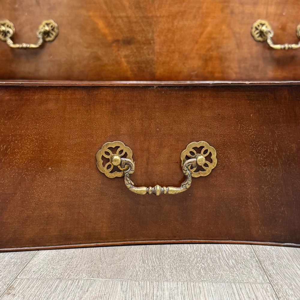 A mahogany serpentine chest of drawers featuring four graduating drawer tiers with brass handles and a curved front profile. View XI