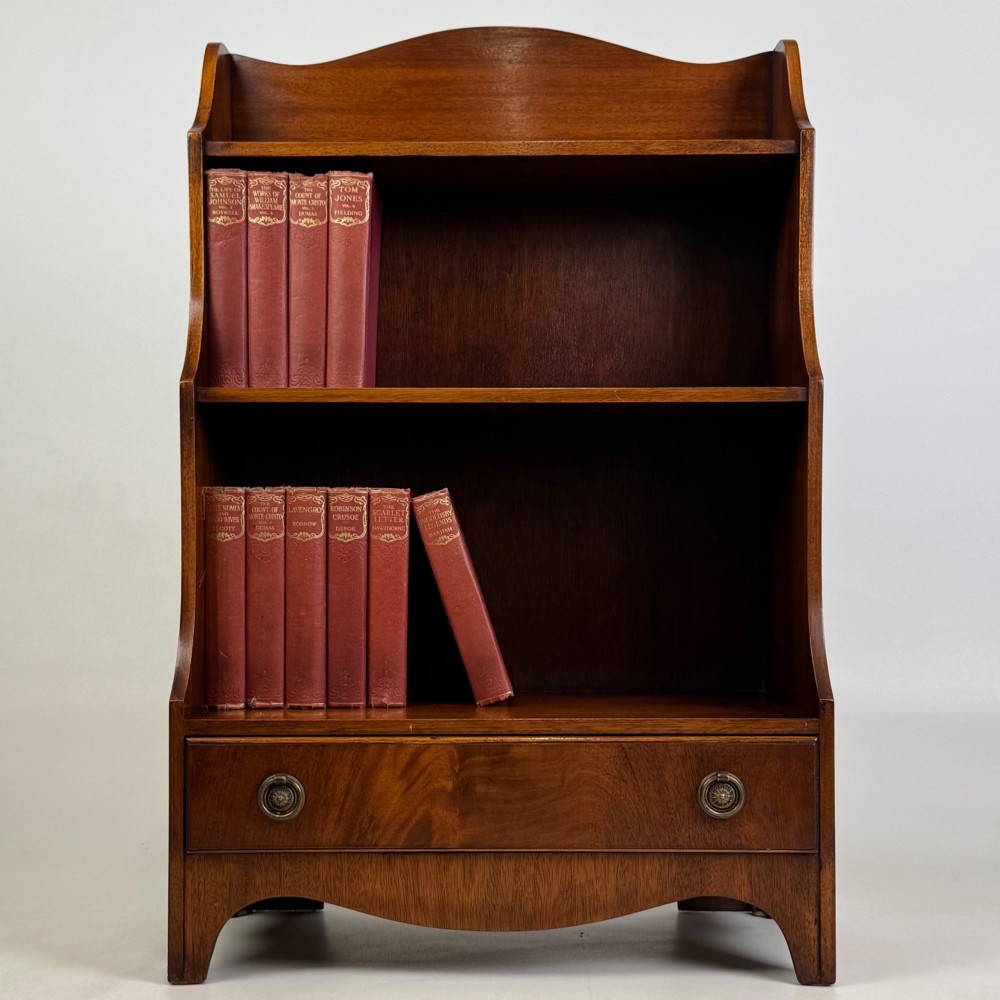 A small 20th-century mahogany open bookcase with a shaped top gallery, two open shelves, and a single lower drawer fitted with brass ring handles.