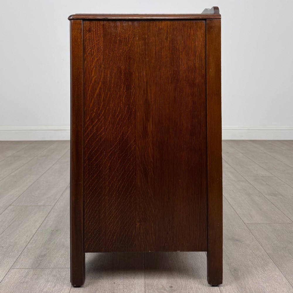A dark brown oak chest of drawers featuring three wide drawers with ornamental metal drop handles and a carved geometric frieze along the top edge. View III