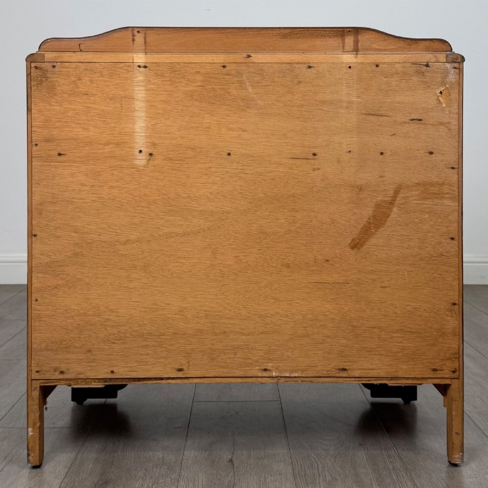 A dark brown oak chest of drawers featuring three wide drawers with ornamental metal drop handles and a carved geometric frieze along the top edge. View V