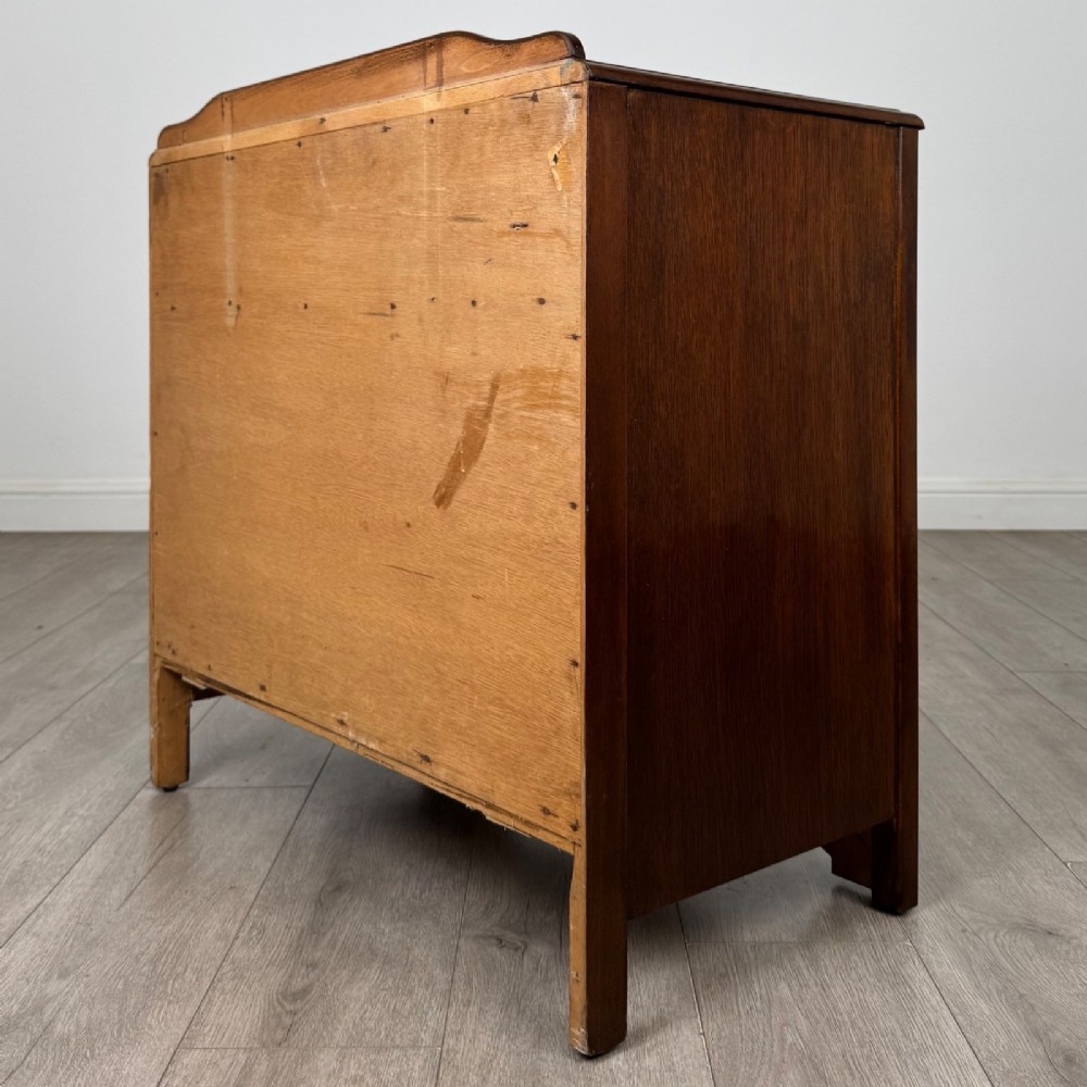 A dark brown oak chest of drawers featuring three wide drawers with ornamental metal drop handles and a carved geometric frieze along the top edge. View VI