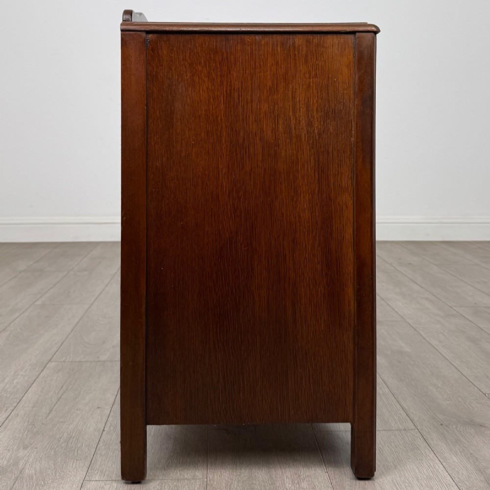A dark brown oak chest of drawers featuring three wide drawers with ornamental metal drop handles and a carved geometric frieze along the top edge. View VII