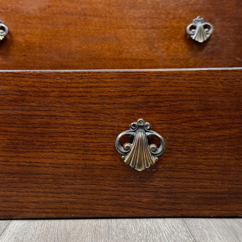A dark brown oak chest of drawers featuring three wide drawers with ornamental metal drop handles and a carved geometric frieze along the top edge. View XI
