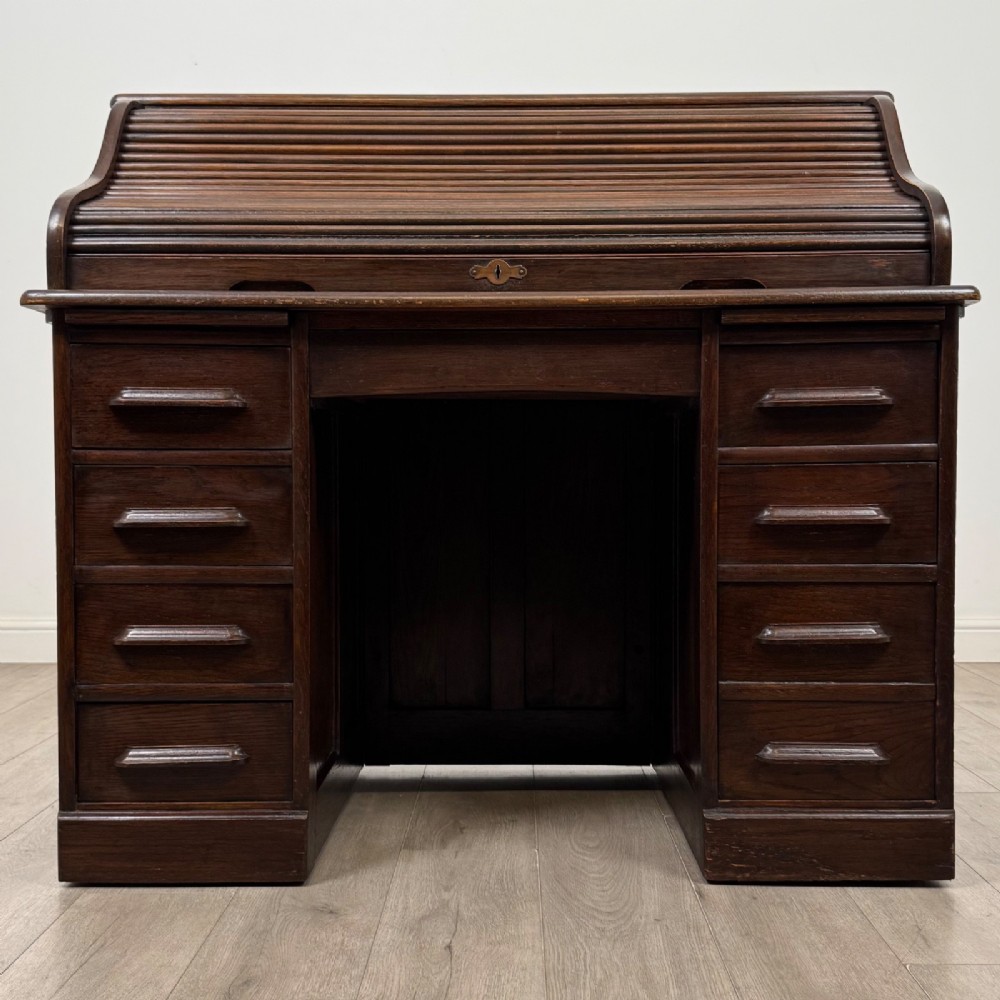 An Edwardian dark oak roll top desk featuring a slatted tambour front above a twin pedestal base with eight drawers.