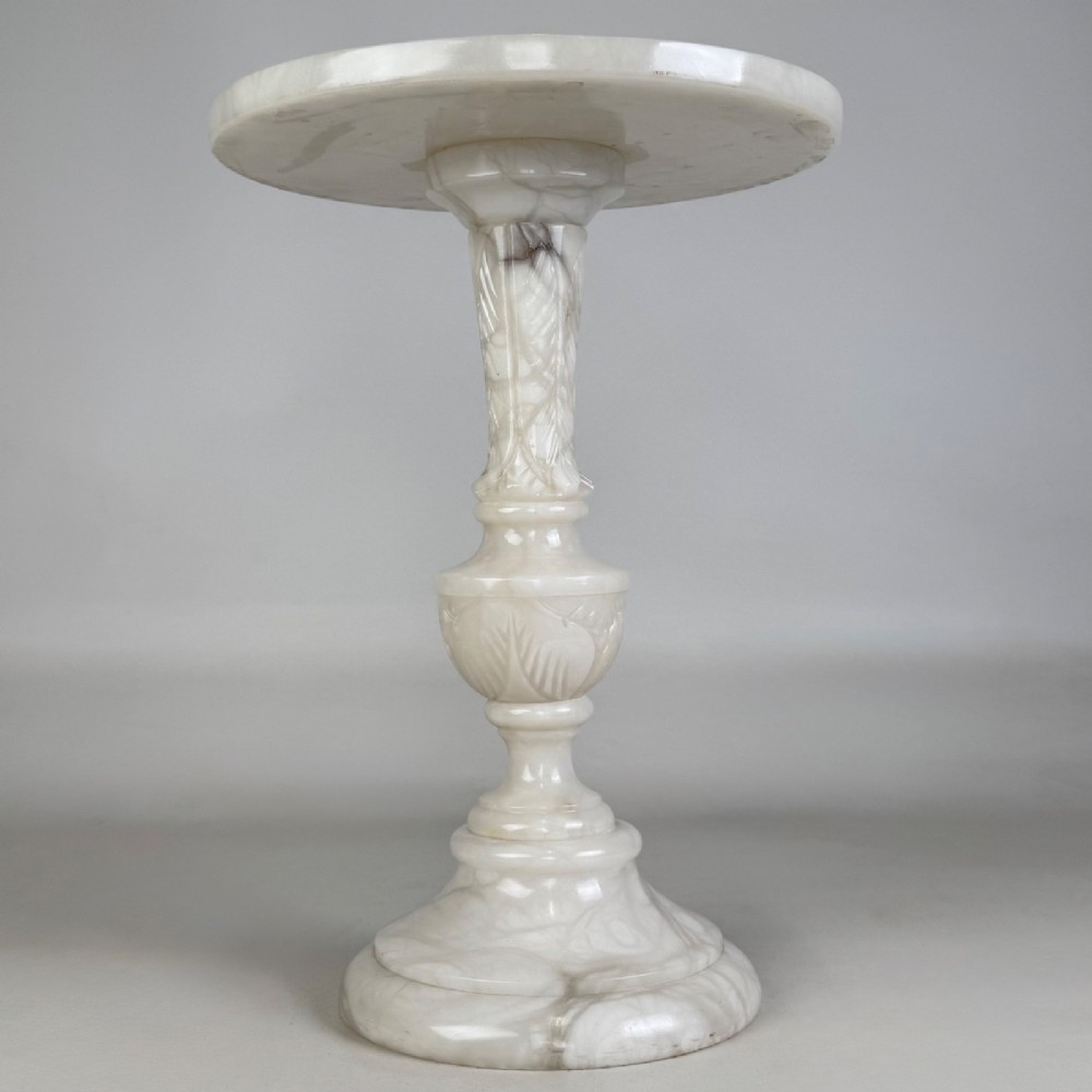 A carved white alabaster side table featuring a circular top resting on a decorative turned pedestal stem and round base.