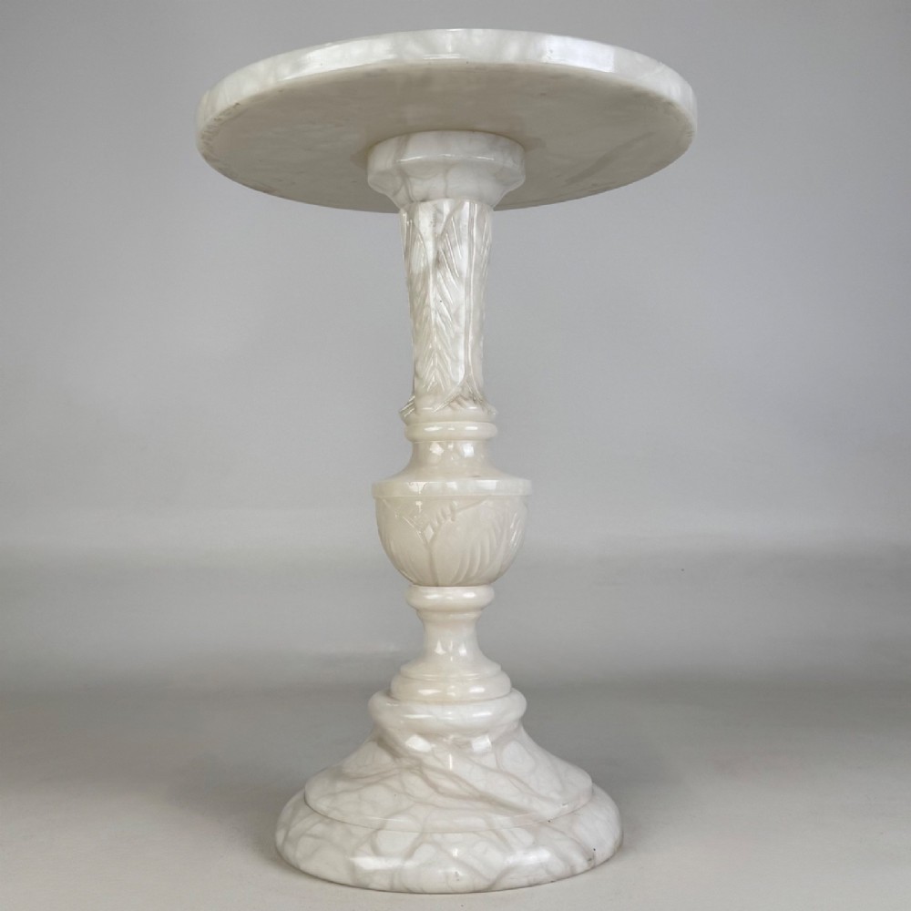 A carved white alabaster side table featuring a circular top resting on a decorative turned pedestal stem and round base. View II
