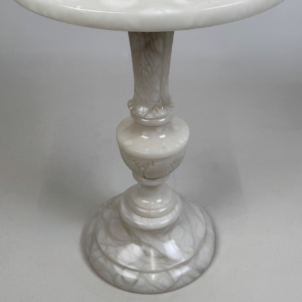 A carved white alabaster side table featuring a circular top resting on a decorative turned pedestal stem and round base. View V